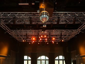 Großer Second-Hand-Kleidungsmarkt in einer Veranstaltungshalle mit rotem Teppich, zahlreichen Ständen mit Kleidungsständern und Besuchern