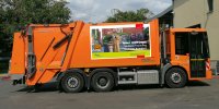 Orangefarbenes Müllfahrzeug mit Plakat "Tatort Biotonne", seitliche Ansicht auf Parkplatz.