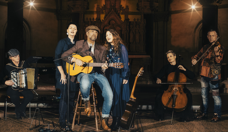 Fünf Personen musizieren gemeinsam in einem Raum mit Gitarre, Akkordeon und Cello.