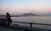 Sonnenuntergang an einer Promenade mit Meerblick und einem Vulkan im Hintergrund.