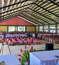Versammlung von Personen in rosa und blauen Uniformen in einer weitläufigen, überdachten Mehrzweckhalle.