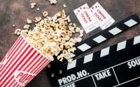 Kinozubehör – rot-weiße Popcorntüte, zwei Eintrittskarten und eine Filmklappe auf dunklem Untergrund.