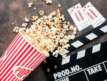 Copyright: Pixelshot Kinozubehör – rot-weiße Popcorntüte, zwei Eintrittskarten und eine Filmklappe auf dunklem Untergrund.