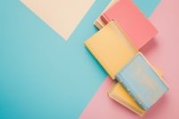 Stapel pastellfarbene Bücher liegen auf pastellfarbenem Untergrund