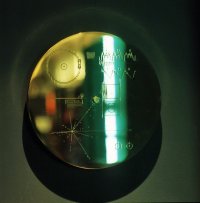 Die goldene Voyager-Schallplatte mit gravierten Diagrammen und einem grünen Lichtreflex auf dunklem Hintergrund.