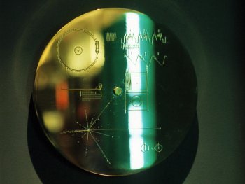 Die goldene Voyager-Schallplatte mit gravierten Diagrammen und einem grünen Lichtreflex auf dunklem Hintergrund.