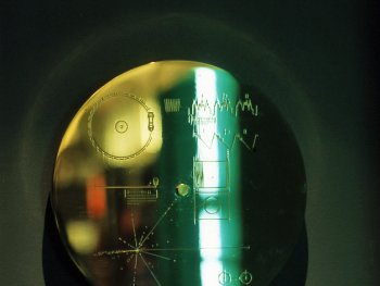 Die goldene Voyager-Schallplatte mit gravierten Diagrammen und einem grünen Lichtreflex auf dunklem Hintergrund.