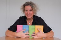 Lächelnde Person mit grau-blonden Locken präsentiert vier bunte Bücher
