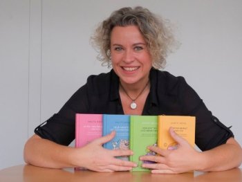 Lächelnde Person mit grau-blonden Locken präsentiert vier bunte Bücher