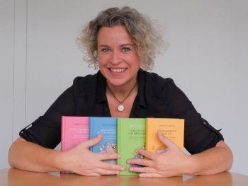 Lächelnde Person mit grau-blonden Locken präsentiert vier bunte Bücher