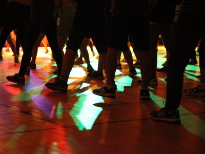 Beine und Turnschuhe mehrerer Personen auf einer Tanzfläche, die von bunten Discolichtern in Rot, Grün und Blau beleuchtet wird.