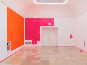 Foto: Foto: Lukas Pürmayr; © VG Bild-Kunst Bonn, 2026
Ausstellungsraum mit orange und pink bemalten Wandflächen, kleinen, farbigen Kunstobjekten aus Silikon an der rechten Wand und Farbspuren auf dem Fliesenboden.