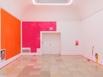 Copyright: Ausstellung "ibid. 30 Positionen aktueller Malerei", Kunsthalle Nürnberg, 4. Juli bis 4. Oktober 2026 Liza Dieckwisch: Eitempera, Silikon, Pigment, Atelierreste, Folie, Stoff (bedruckt), Glitzer, 2026 Ausstellungsraum mit orange und pink bemalten Wandflächen, kleinen, farbigen Kunstobjekten aus Silikon an der rechten Wand und Farbspuren auf dem Fliesenboden.
