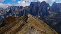 Wandergruppe folgt einem schmalen Pfad entlang eines Grasgrats vor schroffen, zerklüfteten Gebirgsgipfeln.