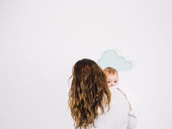 Foto: freepik.com
Person hält schlafendes Baby auf der Schulter vor weißer Wand mit mintfarbener Wolken-Dekoration.