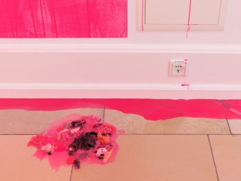 Copyright: Liza Dieckwisch: Eitempera, Silikon, Pigment, Atelierreste, Folie, Stoff (bedruckt), Glitzer, 2026 und pink premium puke, 2026 © VG Bild-Kunst Bonn, 2026 Foto: Lukas Pürmayr Pinke Farbe tropft an einer Wand über einen Sicherungskasten und eine Steckdose auf den Fliesenboden, dort ist eine Ansammlung von Stoffresten und Müll in pinkfarbiges Silikon gegossen.