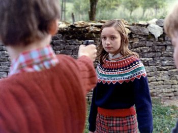 Copyright: Les Films du Losange Ein Mädchen mit gemustertem Pullover und Schottenrock steht vor einer Trockensteinmauer und eine PErson vor ihr hält eine Pistole auf sie.