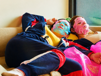 Copyright: Excellent Friends
Zwei Personen mit bunten Gesichtsmasken liegen entspannt auf einer Couch, umgeben von pinken Folienstoffen.