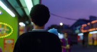 Person von hinten auf einer abendlichen Marktstraße mit bunten Neonlichtern und lila Abendhimmel.
