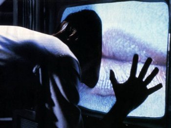Copyright: Filmverleih Eine Person beugt sich in einer dunklen Szene mit einer Hand an einen alten Röhrenfernseher, dessen Bildschirm statisches Rauschen zeigt.