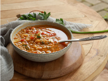 Copyright: Stadtteilzentrum Die Villa Eine Schale mit Linsen-Tomaten-Suppe steht mit Löffel auf einem Holzbrett, garniert mit frischem Koriander.