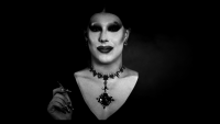 Person in aufwendigem Gothic-Drag-Make-up mit schwarzem Augen-Make-up, Schmuckkette und langen Nägeln in schwarz-weißer Porträtaufnahme.