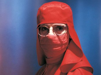 Copyright: Filmverleih Person in einem vollständig roten Schutzanzug mit Haube, Gesichtsmaske und Brille blickt frontal in die Kamera.