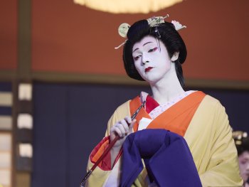 Copyright: SHUICHI YOSHIDAASP_2025 KOKUHO Film Partners Person in traditioneller japanischer Kabuki-Kostümierung mit weißer Gesichtsschminke, gelbem Kimono und aufwendiger Kopfbedeckung hält einen Fächer.