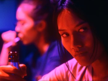 Copyright: eksystent Filmverleih Eine Person hält eine Bierflasche und blickt skeptisch zur Seite, im Hintergrund trinkt eine weitere Person in rotem und blauem Neonlicht.