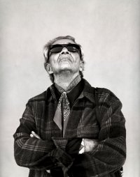 Chavela mit Sonnenbrille und karierter Jacke, Arme verschränkt, Blick nach oben gerichtet.