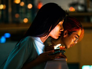 Copyright: 2026 eksystent Filmverleih
Zwei Personen schauen bei Nacht gemeinsam konzentriert auf ein leuchtendes Smartphone-Display vor einer unscharfen Stadtkulisse mit Lichtern.