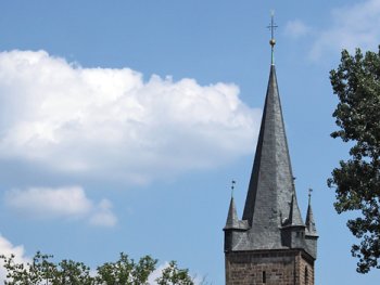 Ein blauer Himmel mit Wolken und einer Kirchturmspitze.