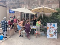 Mehrere Personen und Kinder arbeiten an einem Kreativ-Workshop-Stand der „Werkstadt Nürnberg" im Freien, begleitet von einer freudig posierenden Person.