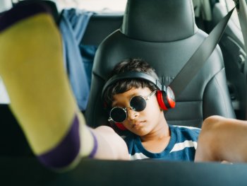 Copyright: Aditya Varma
Kind mit roter Kopfhörern und runden Sonnenbrille lehnt entspannt auf dem Rücksitz eines Autos, während gelb-lila Socken in den Vordergrund ragen.