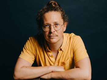 Person mit Brille und hochgesteckten Locken lehnt die Arme auf einem vintage Philips-Tonbandgerät (4404 Stereo, 4-Track) und blickt ruhig in die Kamera.