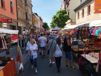 Copyright: ZiMa Zirndorf Marketing eG Menschen schlendern an Marktständen mit Taschen und Kleidung in einer belebten Fußgängerzone entlang