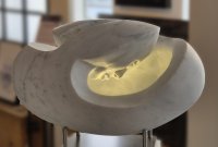 Eiförmige Marmorskulptur mit innen leuchtendem, warmgelbem Licht, das auf ein Gesicht im inneren scheint.