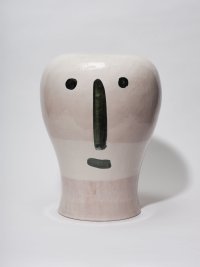 Tonskulptur mit stilisiertem Gesicht aus zwei runden Augen, einer länglichen Nase und einem Mund in schwarzer Farbe.