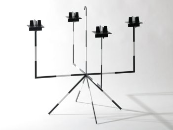 Vierarmiger Kerzenständer aus schwarz-silbern gestreiften Metallstäben mit quadratischen Kerzenhaltern, auf einem vierbeinigen Gestell stehend.