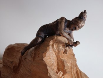 Foto: Matthias Lehr, VNP
Bronzefigur einer Person, die auf einer hölzernen Skulptur rittlinks sitzt und diese bearbeitet.