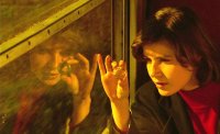 Person mit dunklen Haaren betrachtet an einem Fenster eine kleine Glaskugel zwischen den Fingern in warmem Licht.