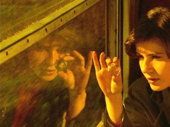 Copyright: Studiocanal
Person mit dunklen Haaren betrachtet an einem Fenster eine kleine Glaskugel zwischen den Fingern in warmem Licht.