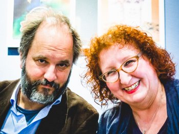 Copyright: Matthias Fetzer Kurzfilmnacht mit Egersdörfer & Schleindl: Ein Mann mit grauem Bart und eine lächelnde Frau mit roten Locken und Brille blicken in die Kamera.