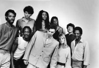 Schwarz-weiß-Gruppenfoto von den Talking Heads, die eng zusammenstehen und in die Kamera blicken.