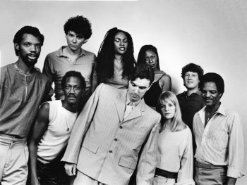 Copyright: Courtesy of Sire and Warner Music Group
Schwarz-weiß-Gruppenfoto von den Talking Heads, die eng zusammenstehen und in die Kamera blicken.
