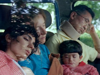 Copyright: Grandfilm Vier Personen sitzen dicht gedrängt mit geschlossenen Augen in einem Fahrzeug, während Licht durch die Fenster fällt.