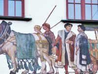 Historisch gekleidete Männer in Pelzmänteln stehen vor einem reich geschmückten Pferdewagen, im Gespräch mit zwei Kutschern; das Pferd ist mit Quasten behangen, im Hintergrund ein überdachter, leerer Holzwagen – Teil eines Wandgemäldes.