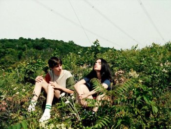 Copyright: Filmverleih
Zwei junge Personen sitzen nebeneinander in einer üppig bewachsenen Wiese mit Sträuchern und Blumen unter freiem Himmel.