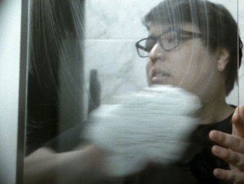Copyright: Denis Côté
Person mit Brille berührt eine Glasscheibe, durch die ihr Gesicht verzerrt und spiegelnd zu sehen ist.