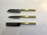 Drei japanische Küchenmesser mit unterschiedlich geformten Klingen und goldfarbenen Griffen liegen parallel nebeneinander auf einer weißen Fläche.